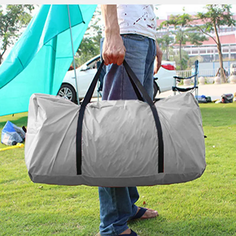 Person holding a gray duffel bag outdoors with a tent and car in the background