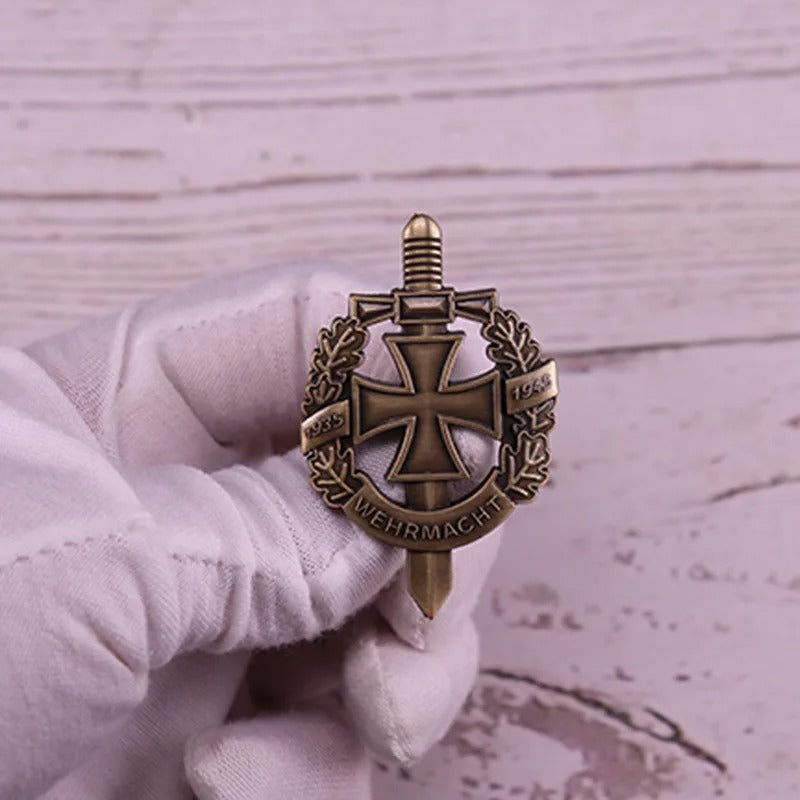 Gloved hand holding brass Wehrmacht badge with Iron Cross and sword on wreath German Luftwaffe badges