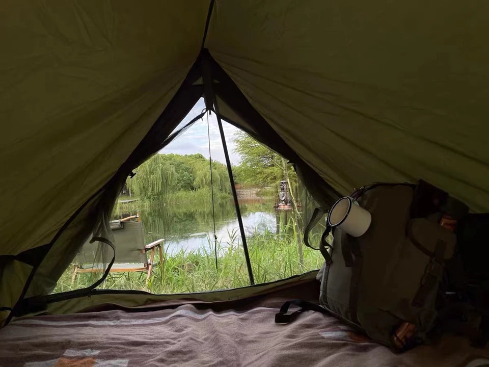View from inside olive drab military camping tent overlooking a lakeside chair with backpack and enamel mug inside
