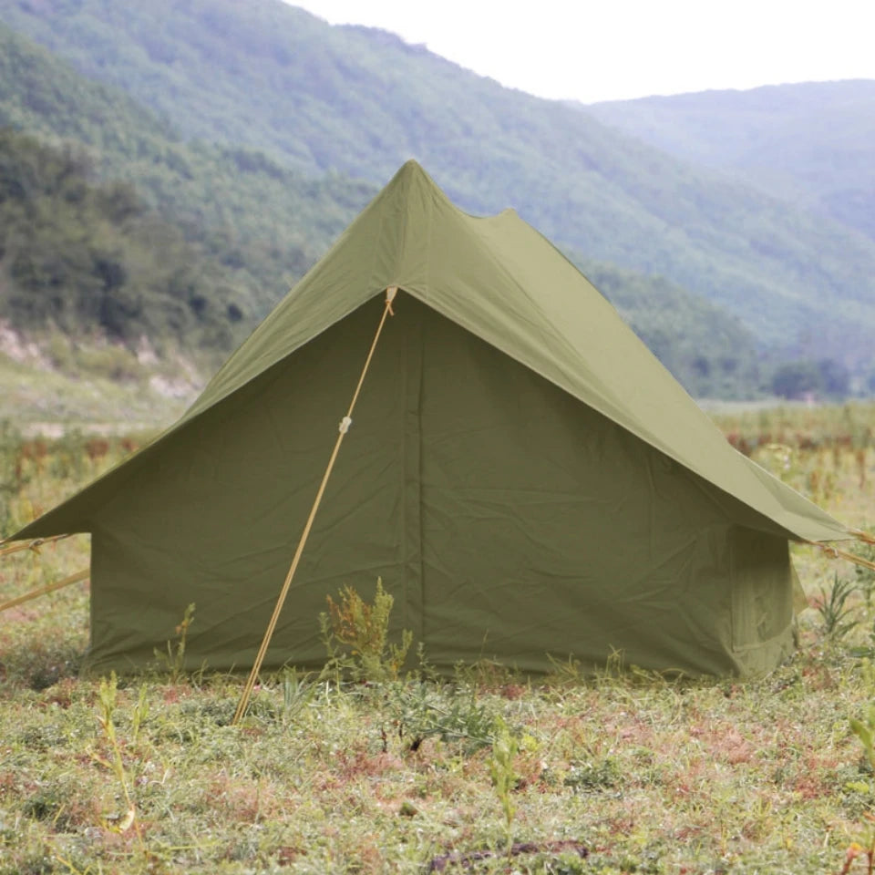 Olive green military camping tent a frame pitched in grassy field with mountain backdrop