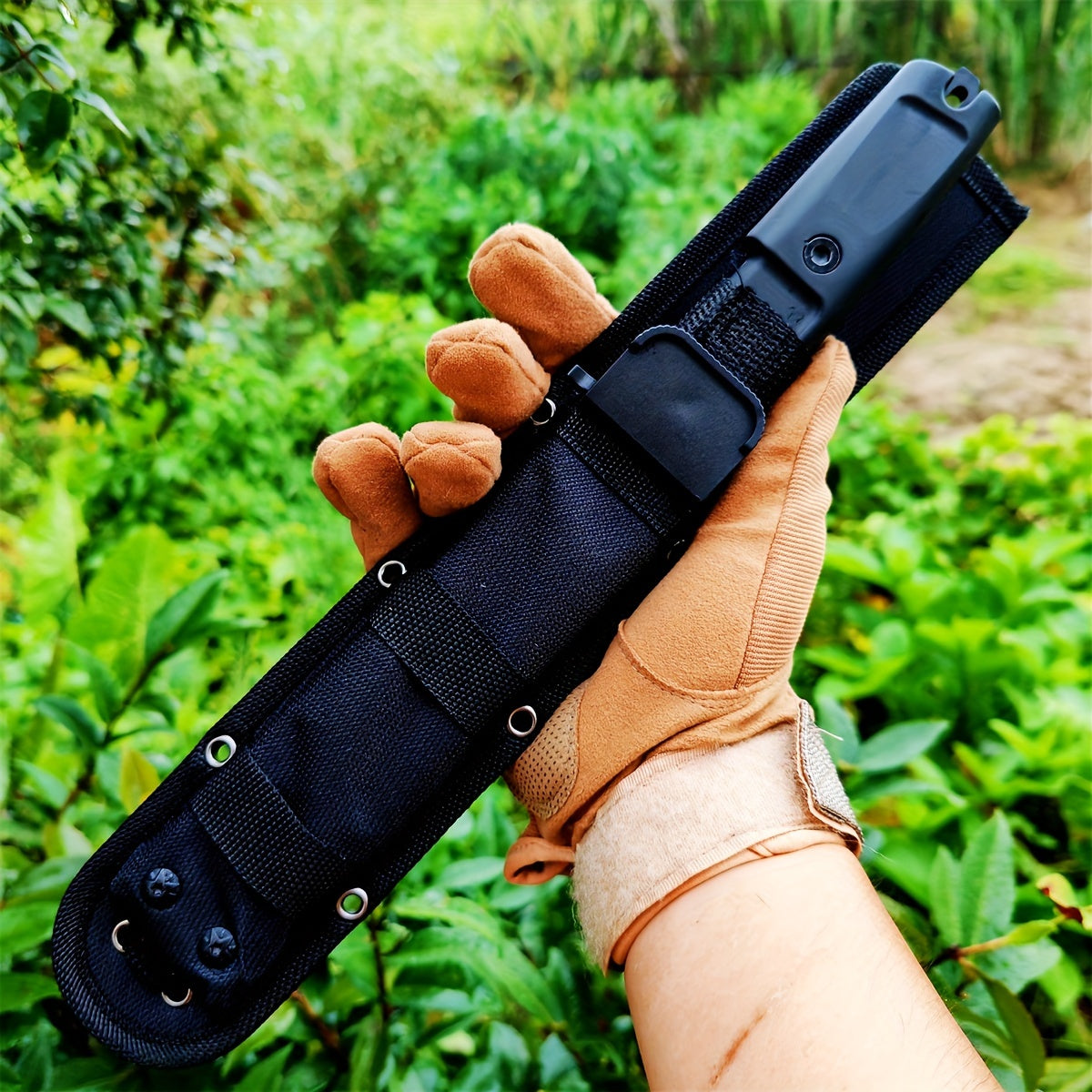 Gloved hand holding tactical black sheath with knife handle in forest setting wilderness survival multi-purpose knife