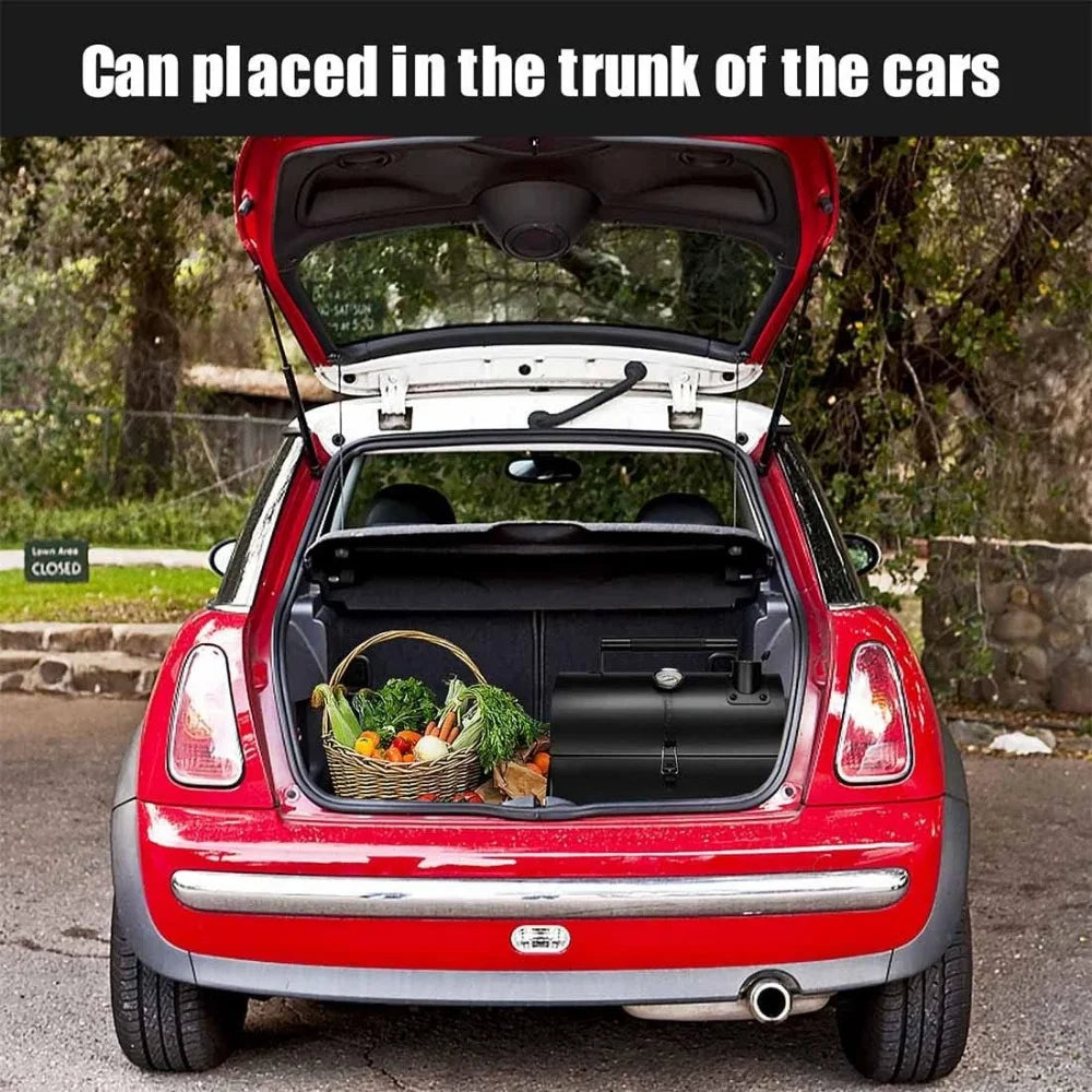 Portable charcoal grill placed in the trunk of a red car next to a basket of vegetables