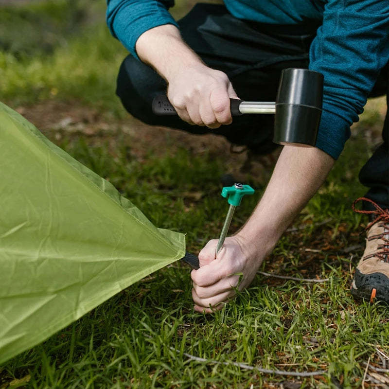 User using a rubber mallet hammer to secure a tent stake into the ground
