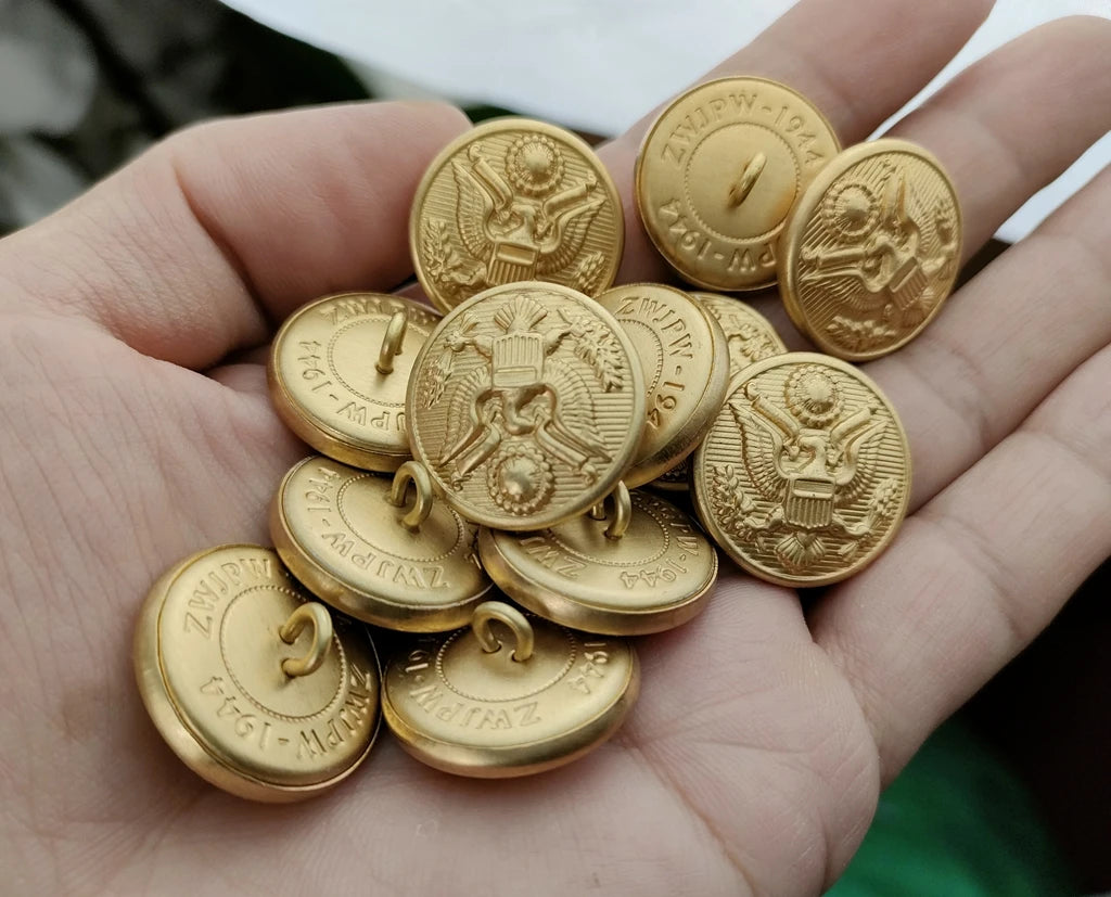 A hand holding WWII US Army uniform buttons featuring detailed eagle design in antique gold finish