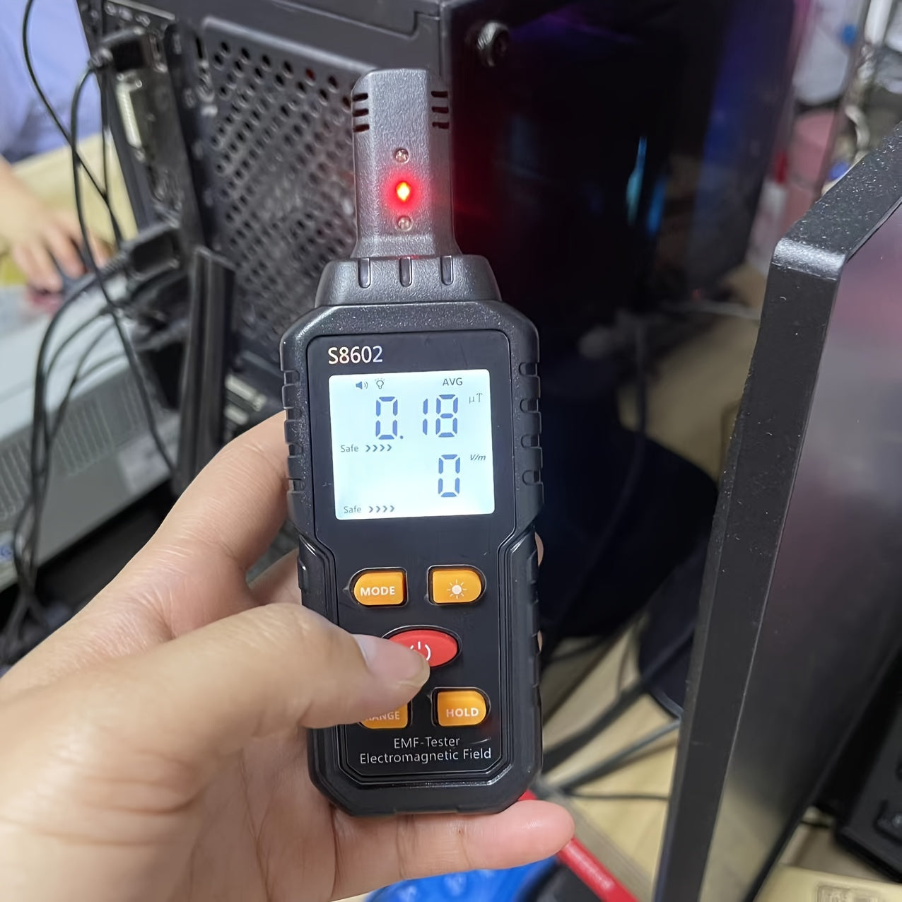 Hand holding EMF meter for home use measuring electromagnetic field near computer equipment
